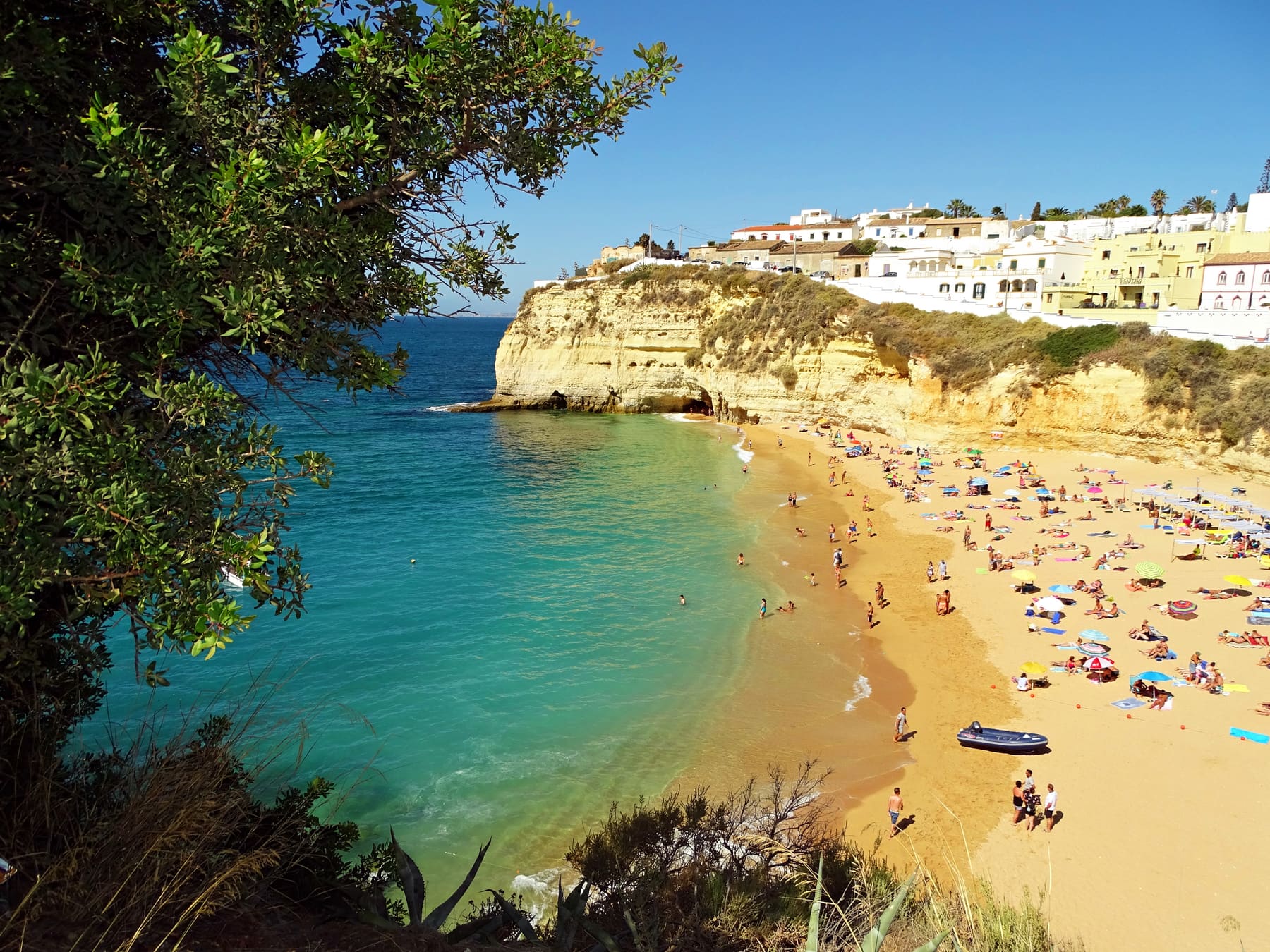 Praia do Carvoeiro: a sandy cove with swimmers and sunshades below white village houses on the cliff.